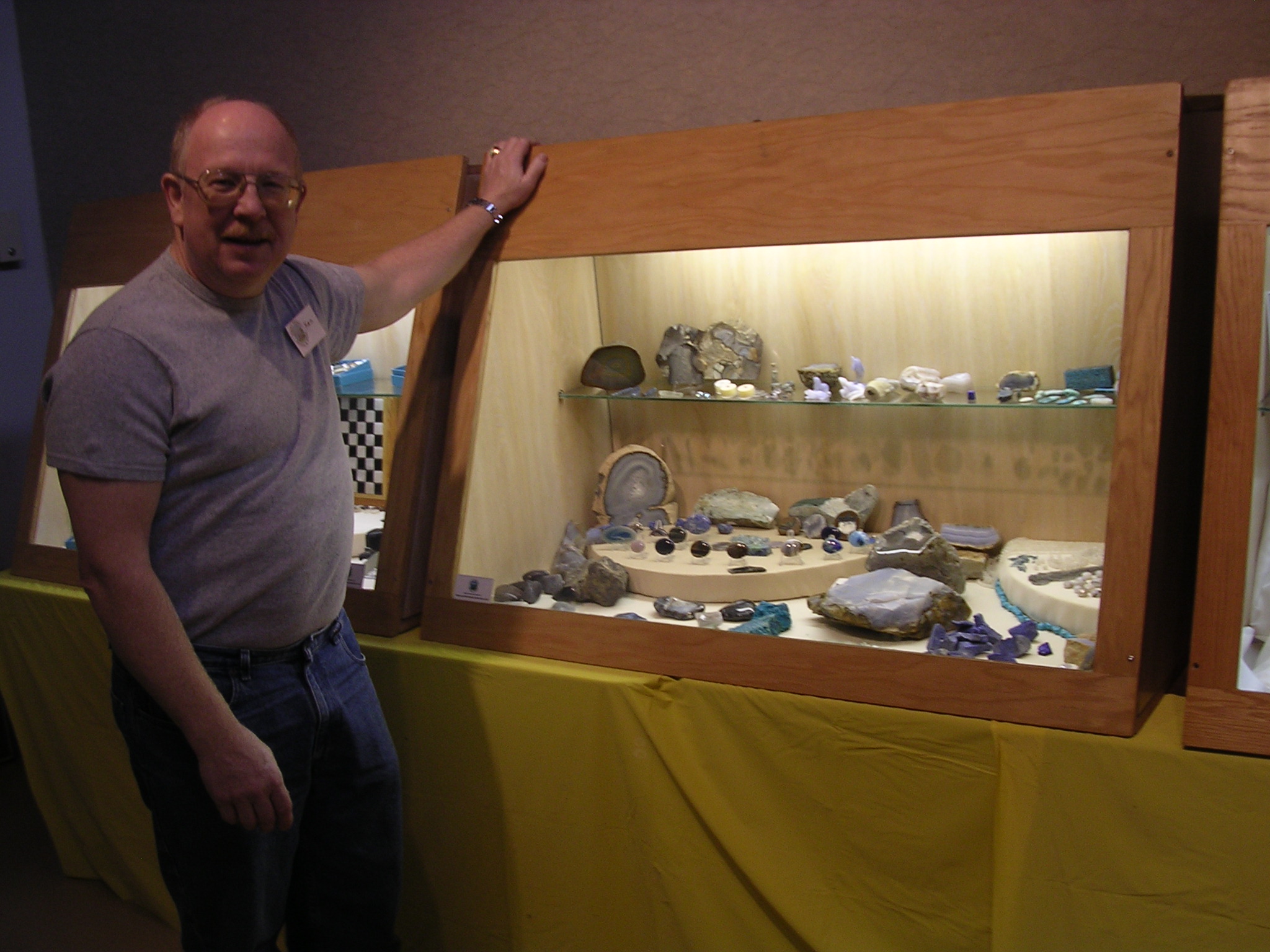 Club member beside an illuminated display of rocks, minerals and lapidary work at the 2006 Rock Oddities show.
